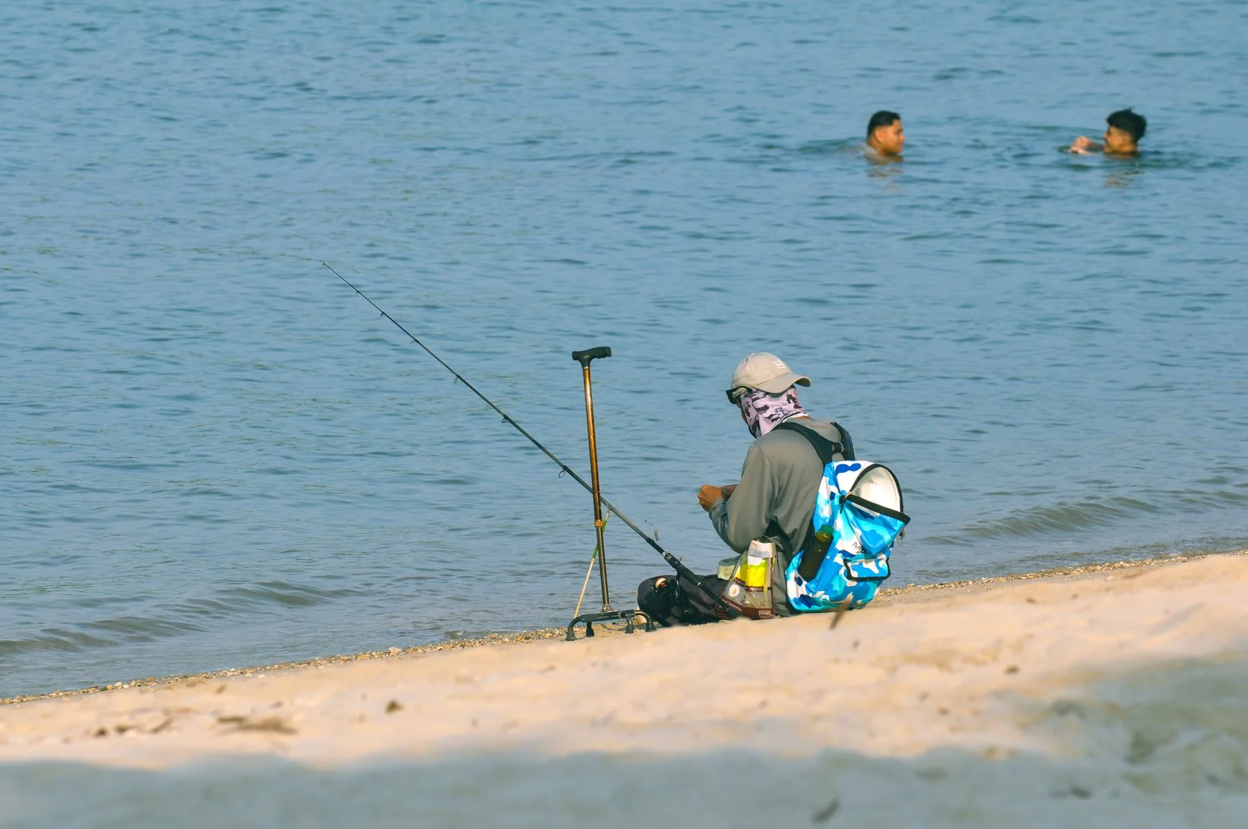 An angler seated on sand holding a fishing rod